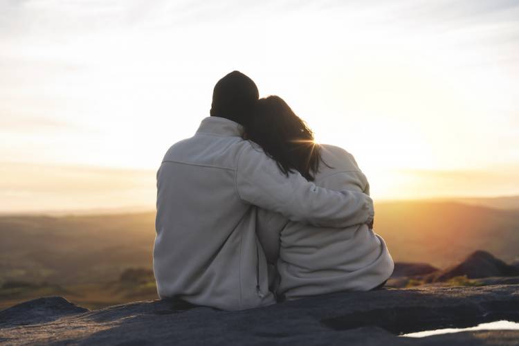 couple hugging as they sit and overlook the sunset in the mountains